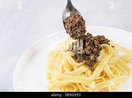 A spoon of savory black truffle sauce being added to a bowl of fresh pasta. Perfect for a gourmet culinary experience, capturing the essence of Italia Stock Photo