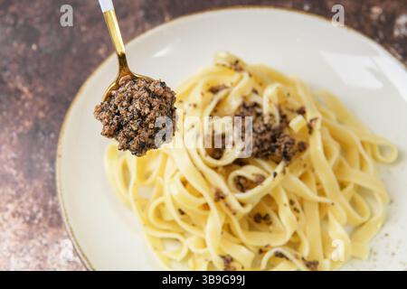 Tagliatelle pasta with chopped black truffle on the spoon, selective focus. Fresh Italian autumn recipe with black truffle on brown table in elegant r Stock Photo