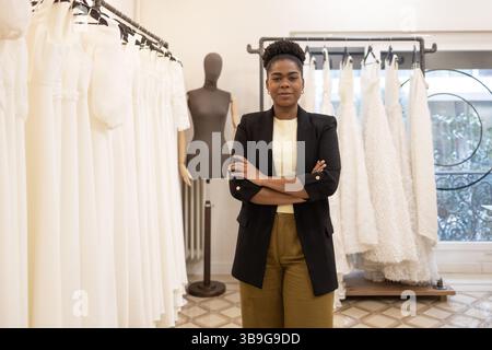 A confident fashion designer stands amidst elegant bridal gowns in a stylish atelier, exuding professionalism and creativity. Mannequin and dresses en Stock Photo