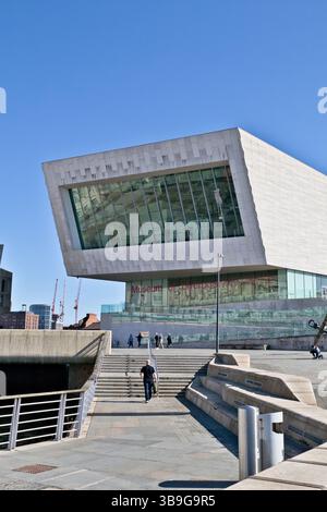 Museum of Liverpool with an angled facade, large glass windows, clear blue sky, and a man walking up the steps toward the entrance. Stock Photo