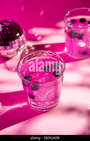 Refreshing iced pink drinks garnished with berries sits in a glass on a vibrant pink surface. The soft lighting and shadows add a festive and stylish Stock Photo
