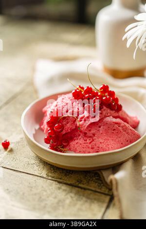 Homemade pink berry mousse garnished with fresh red currants in a ceramic bowl on a tiled table, creating a vibrant food scape. Stock Photo