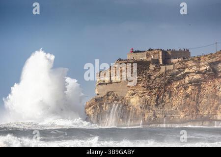 View of the cliffs and the Farol de Nazare lighthouse. Very high waves crash against the coast, Leiria, Portugal Stock Photo