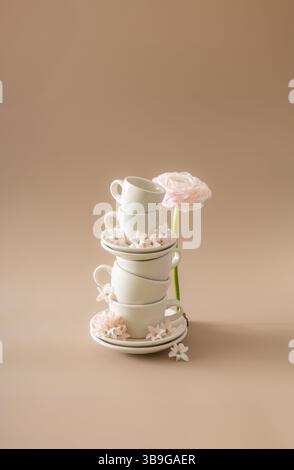 Aesthetic composition of white ceramic cups stacked with delicate spring flowers on a beige surface, evoking a serene, springtime aesthetic. Stock Photo