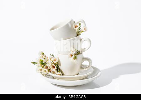 Delicate arrangement of stacked white cups adorned with fresh spring flowers, all set against a stark white background, enhancing the minimalist aesth Stock Photo