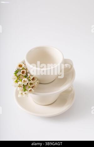 Elegant white teacups neatly stacked with saucers, adorned with fresh white spring flowers on a clean background, conveying a serene and aesthetic vib Stock Photo