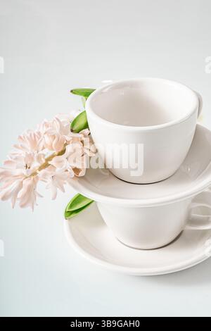 Elegant white cups stacked with a delicate pink hyacinth flower and green leaves on a soft background, symbolizing spring freshness and minimalist tab Stock Photo