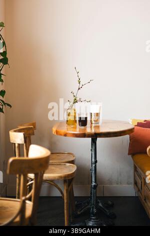 A cozy cafe corner featuring a wooden table with a decorative vase and drinks, surrounded by wooden chairs. Soft natural light creates a warm, invitin Stock Photo