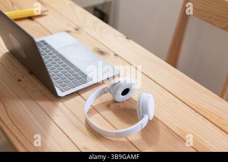 A minimalist workspace with a sleek laptop and white headphones on a light wooden desk. Ideal for representing modern work, technology, and productivi Stock Photo