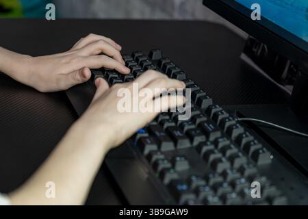 Close-up of a teenage boy's hands on a keyboard while gaming, emphasizing focus and involvement in a digital environment. The image captures the essen Stock Photo
