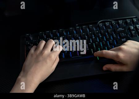 A close-up view of teen hands on a glowing keyboard in a dark, immersive gaming setup, highlighting the focus and intensity of the gaming experience Stock Photo