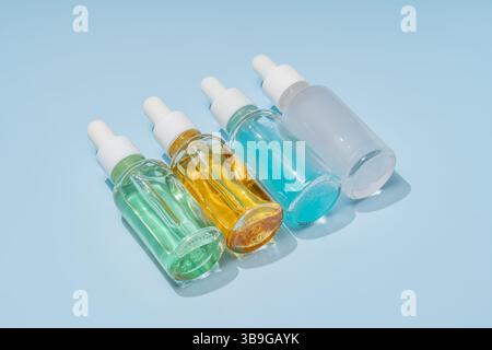 A set of four glass dropper bottles filled with colored liquids, arranged diagonally on a bright blue surface. Ideal for skincare, beauty, or essentia Stock Photo