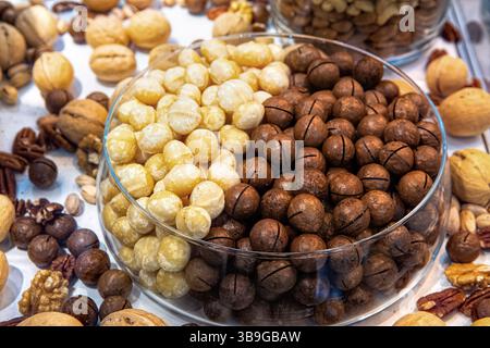 Macadamia nuts in glass bowl among other various nuts in health food store display case. Mixed nuts background. Stock Photo