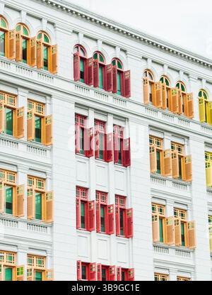 Vibrant red, yellow, and green window shutters contrast against the crisp white facade of a colonial style building in Singapore, showcasing architect Stock Photo