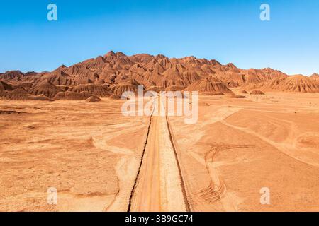 A solitary dirt road stretches through a vast, arid desert landscape leading towards striking, rugged mountains under a clear blue sky in the argentin Stock Photo