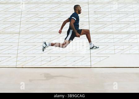 Dynamic image of a black male athlete in mid-air with a backdrop of geometric urban design, showcasing strength, energy, and modern athleticism. Stock Photo