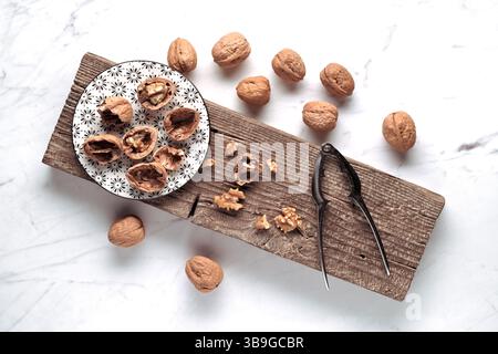 A rustic setup features whole and cracked walnuts on a patterned plate, with a nutcracker beside them, all displayed on a wooden board. A simple, natu Stock Photo