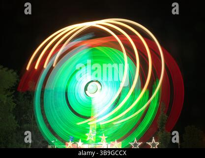 Vibrant long exposure photograph capturing the movement of colored lights at a festive nighttime setting, showcasing a stunning swirl of green and red Stock Photo