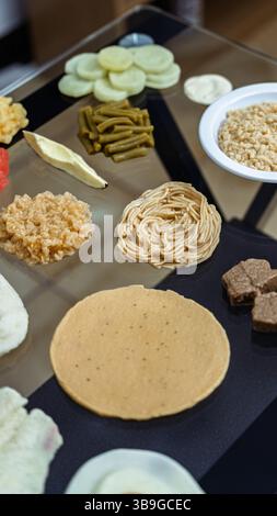 An assortment of food samples laid out in a nutritionist's office. Includes pasta, fruits, vegetables, and grains arranged on a glass table, creating Stock Photo