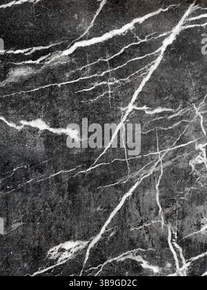 Close-up of a dark marble surface with intricate white veins running through it, showcasing natural patterns and textures ideal for backgrounds, desig Stock Photo