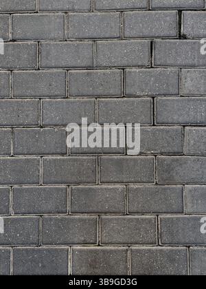 A close-up view of a dark stone brick wall, showcasing its rough texture and the pattern formed by rectangular bricks. Ideal for backgrounds in archit Stock Photo