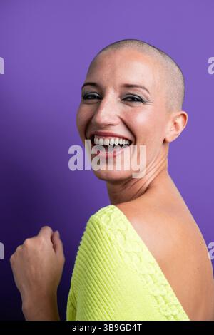 A vibrant portrait of a middle aged woman with a shaved head, smiling brightly against a purple background. The image captures the essence of joy, con Stock Photo
