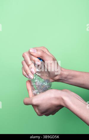 Two hands squeeze a clear plastic bottle, demonstrating recycling and waste reduction. The vibrant green background highlights the environmental focus Stock Photo