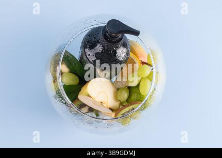 A black pump bottle of shower gel surrounded by fresh fruits and green leaves, inside a glass bowl on a light blue background. Perfect for skincare an Stock Photo