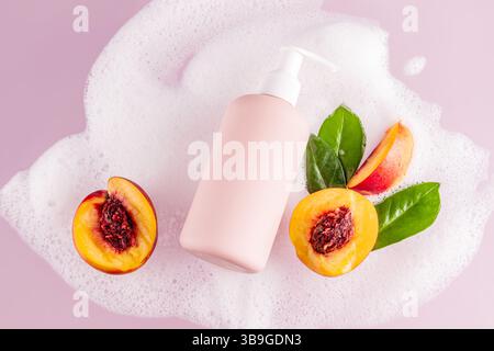 A pink shower gel bottle lies amidst soap bubbles, fresh peach halves, and glossy green leaves on a soft pink background, setting a refreshing and fra Stock Photo