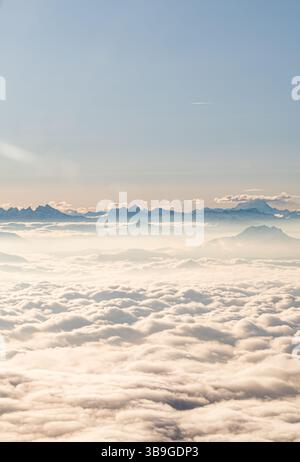 Ethereal aerial photograph showcasing the majestic Alps piercing through a thick blanket of clouds, captured from the air under a clear sky during sun Stock Photo