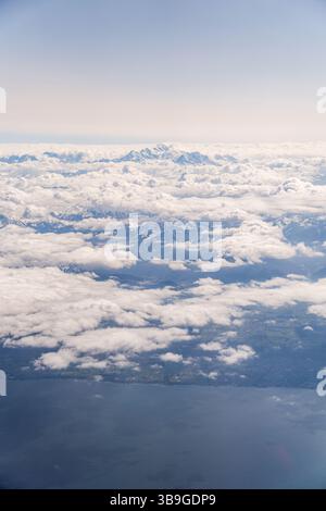 Captivating aerial photograph showcasing the majestic Alps, peaking through a dense layer of clouds, with vibrant sky and land contrasts. Stock Photo