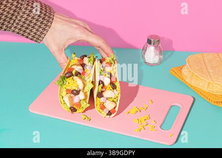 Cropped unrecognizable person holding Mexican tacos filled with chicken, yellow rice, black beans, lettuce, tomatoes, and onions on a colorful pink cu Stock Photo