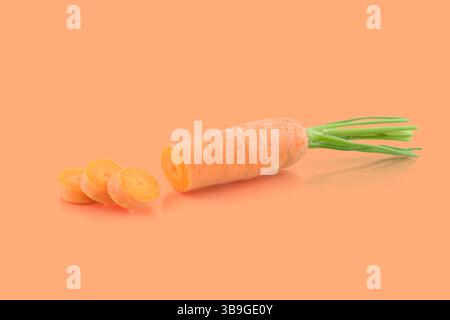 Fresh carrot with green leaves being sliced on a vibrant orange background, showcasing its natural color and texture Stock Photo