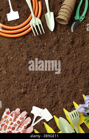 A collection of gardening tools, including a trowel, rake, hose, pruning shears, gloves, and plant markers, arranged on rich soil. Perfect for gardeni Stock Photo