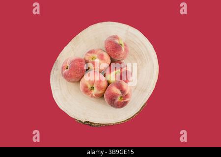 From above freshly picked donuts peaches arranged on a wooden plate, creating a visually appealing contrast against the bold red background Stock Photo