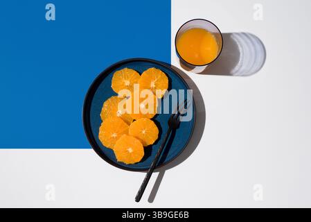 Bright and fresh, sliced oranges are artfully arranged on a blue plate beside a glass of orange juice. The modern geometric background enhances the vi Stock Photo