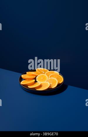 A plate of vibrant orange slices arranged neatly on a dark blue surface. The contrast highlights the freshness of the fruit, creating a visually appea Stock Photo