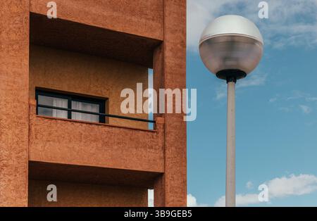 A stunning example of urban design featuring a textured brown building facade with a window and a modern street lamp against a vibrant blue sky dotted Stock Photo