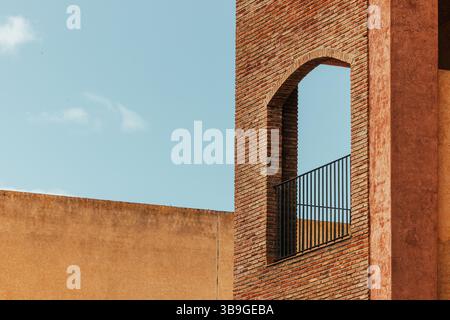 A picturesque image capturing a brick tower with a distinctive arched opening and black metal railing, set against a clear blue sky. The rustic textur Stock Photo