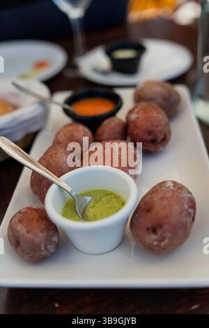 The typical Canarian dish papas arrugadas, crumbly boiled potatoes with green and red sauce (mojo rojo and mojo verde) is served on a plate. Canarian potatoes with a salt crust. Stock Photo