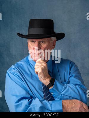 Older caucasian man wearing blue shirt and black hat in contemplative pose Stock Photo