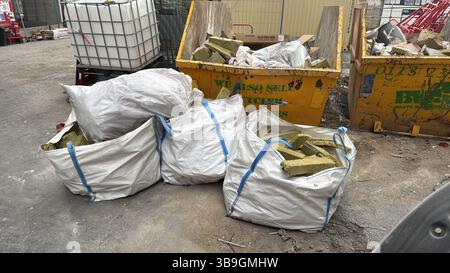Image shows bags and skips filled with construction waste, including insulation and other discarded materials, on a grey concrete surface. Stock Photo