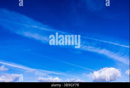Contrails of passing airplanes, cirrus clouds ruffled by the wind in the blue sky Stock Photo