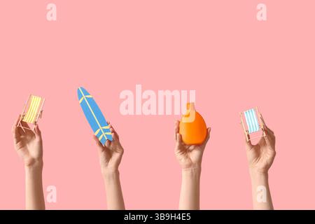 Female hands holding mini deck chairs with surfboard and sunscreen on pink background Stock Photo