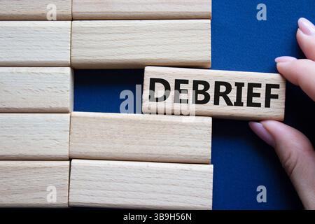 Debrief symbol. Concept word Debrief on wooden blocks. Businessman hand. Beautiful deep blue background. Business and Debrief concept. Copy space. Stock Photo
