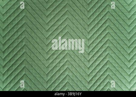 Detailed macro shot of a green textile with a repeating chevron stitch pattern, showing texture, shadows, and perforations on quilted fabric under dif Stock Photo