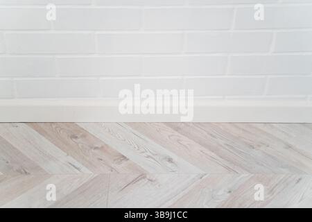 White painted brick wall with soft texture and wooden parquet floor in herringbone pattern. Clean and minimalistic indoor surface ideal for design or Stock Photo