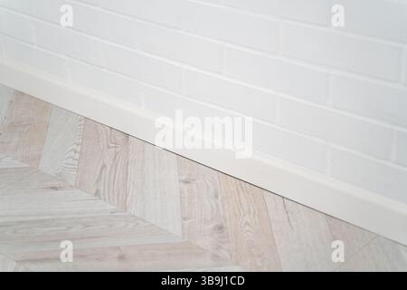Perspective shot of a white painted brick wall and modern wood-patterned laminate floor, capturing clean lines and soft transitions in contemporary in Stock Photo
