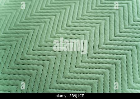 Angled view of quilted green fabric featuring zigzag stitched lines, capturing subtle shadows, detailed texture, and repetitive geometric sewing patte Stock Photo