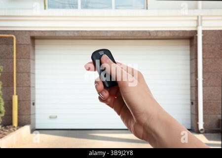 Woman using remote to control garage door outdoors, closeup Stock Photo